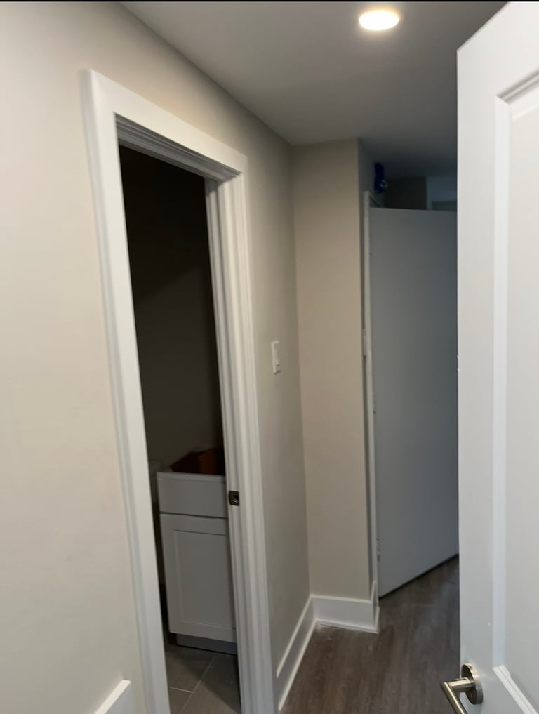 Modern hallway with white walls and dark hardwood flooring, featuring open doorways leading to adjacent rooms