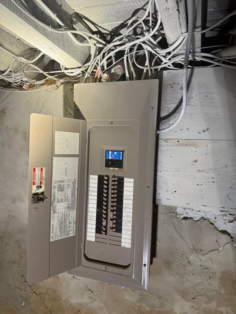 Open electrical panel with circuit breakers and tangled wires above it