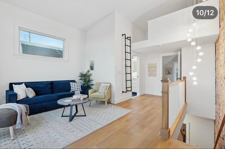 Modern living room with blue sofa, wooden flooring, and loft-style white walls with industrial ladder