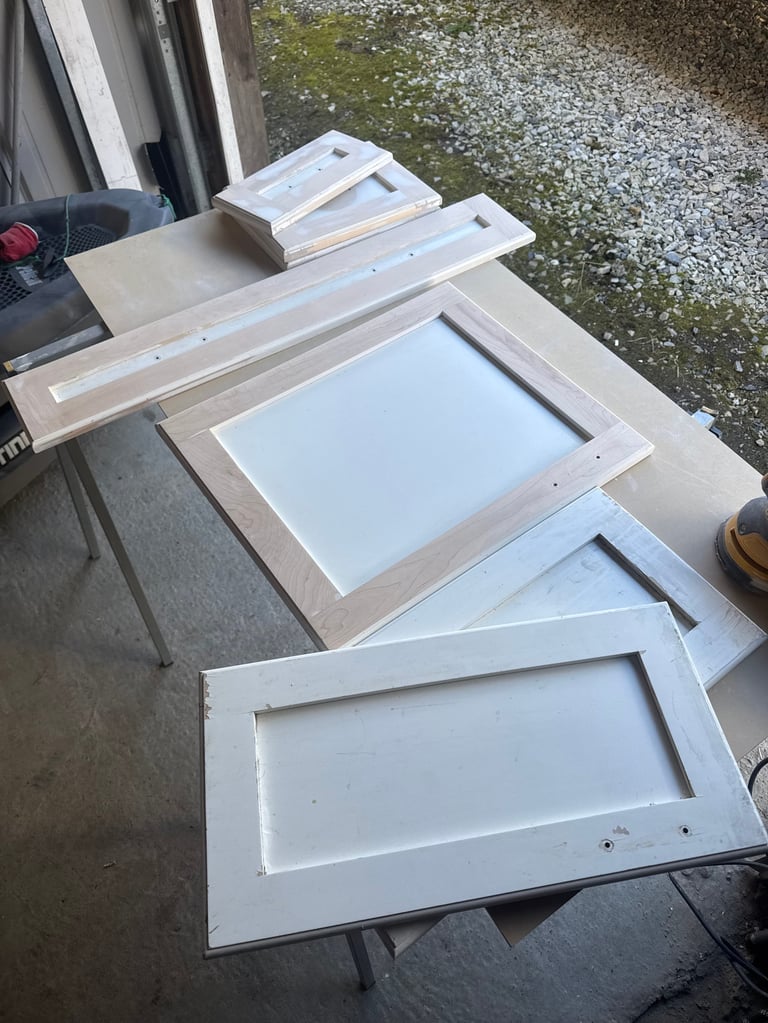 White wooden cabinet door frames and panels arranged on a work table outdoors