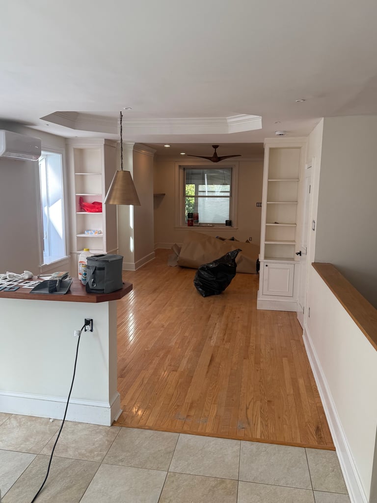 Open-concept home interior with kitchen on left, wooden flooring, cream walls, doorways, and natural lighting from windows