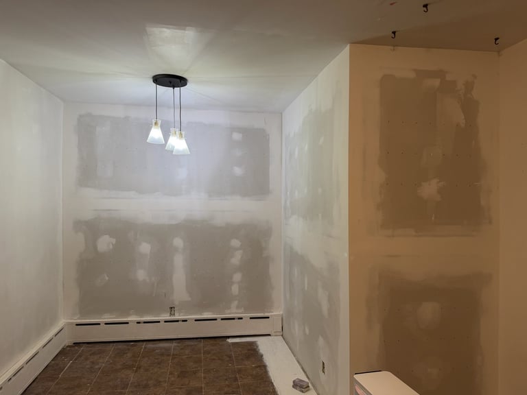 Unfinished kitchen interior with drywall, pending installation, hanging light fixture above, and brown tile flooring