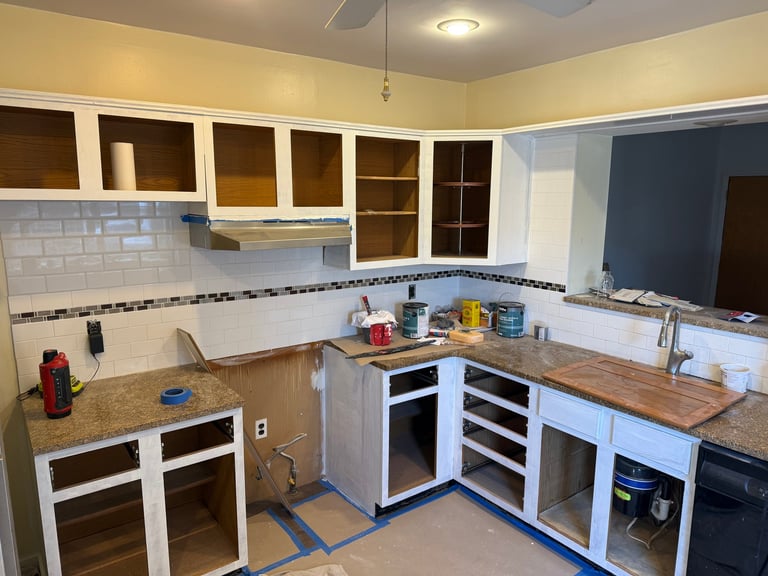 Unfinished kitchen renovation with white cabinetry, brown granite countertops, white subway tile backsplash, and opened cabinet doors revealing shelving