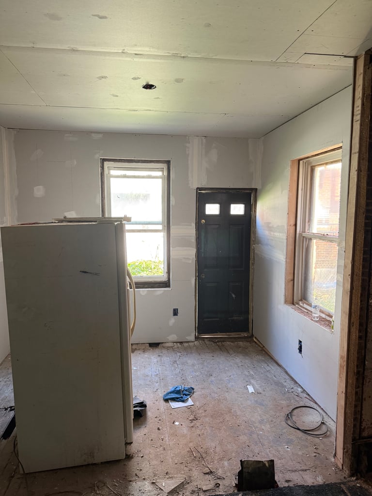 Unfinished kitchen renovation with white refrigerator, black door, and exposed drywall