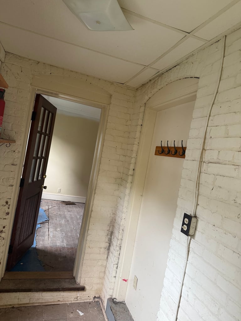 Interior hallway with white painted brick walls, doorway on left, electrical outlet on right wall, and exposed ceiling with ventilation