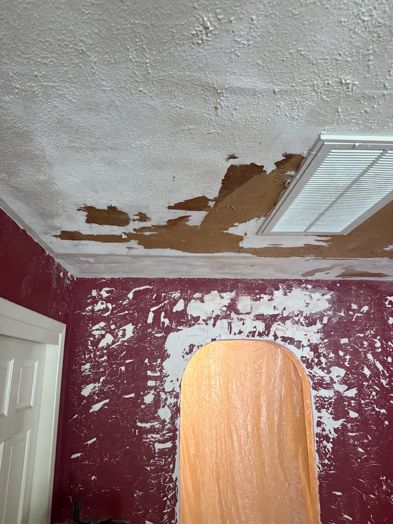 Damaged ceiling with peeling paint and missing plaster sections above burgundy walls in need of repair