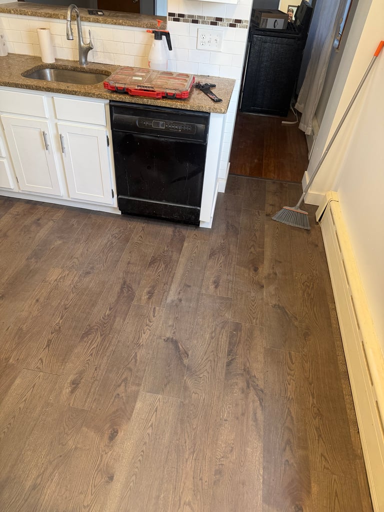 Modern kitchen with white cabinets, black dishwasher, and wood-look flooring viewed from above