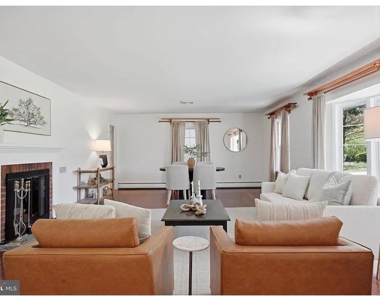 Bright living room with cognac leather armchairs, gray sofa, fireplace, and windows overlooking garden