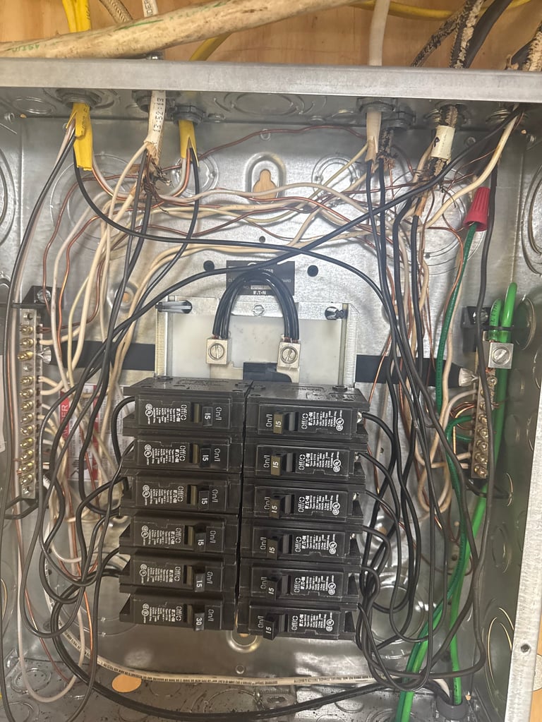 Electrical panel with multiple black circuit breakers and tangled wiring mounted on a metal backing plate