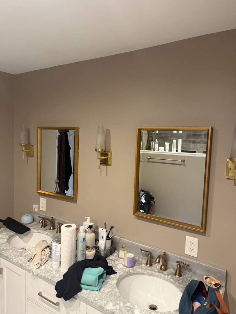 Bathroom vanity with two gold-framed mirrors, marble countertop, and various toiletries and personal items