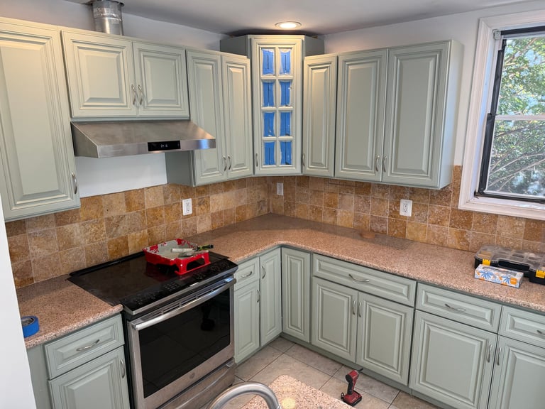 Modern kitchen with mint green cabinets, brown tile backsplash, black stovetop, and stainless steel appliances