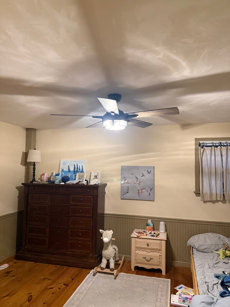 Modern ceiling fan with LED light mounted on textured ceiling in bedroom with wood furniture and beige walls