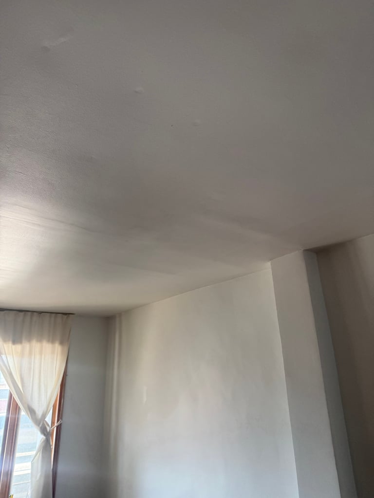 Interior of a room with white walls and ceiling, a window with white curtains on the left side