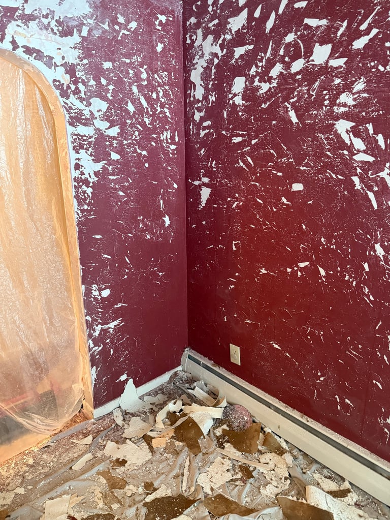 Construction debris and plastic sheeting against burgundy walls with peeling paint in an unfinished room