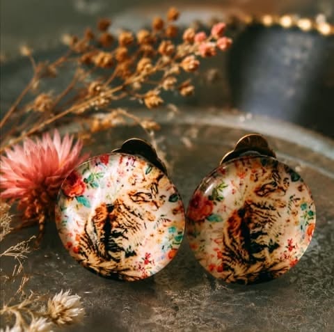 Pair of decorative earrings with floral and nature patterns featuring pink and green accents on cream and brown backgrounds
