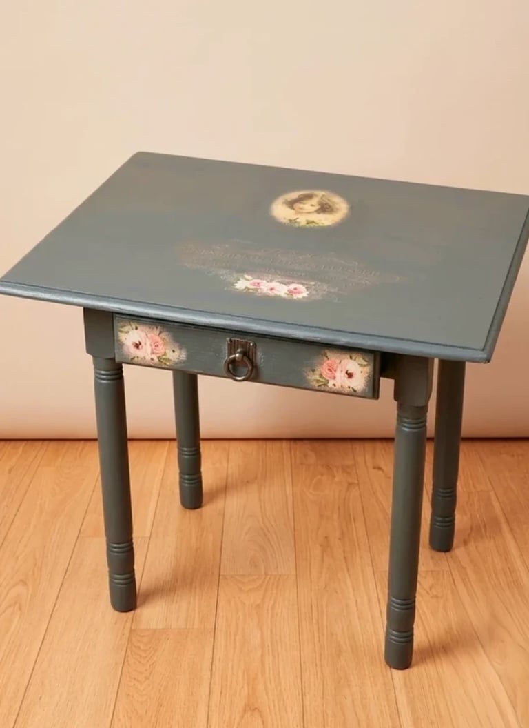 Grey side table with floral decals, drawer, and turned legs on a wooden floor