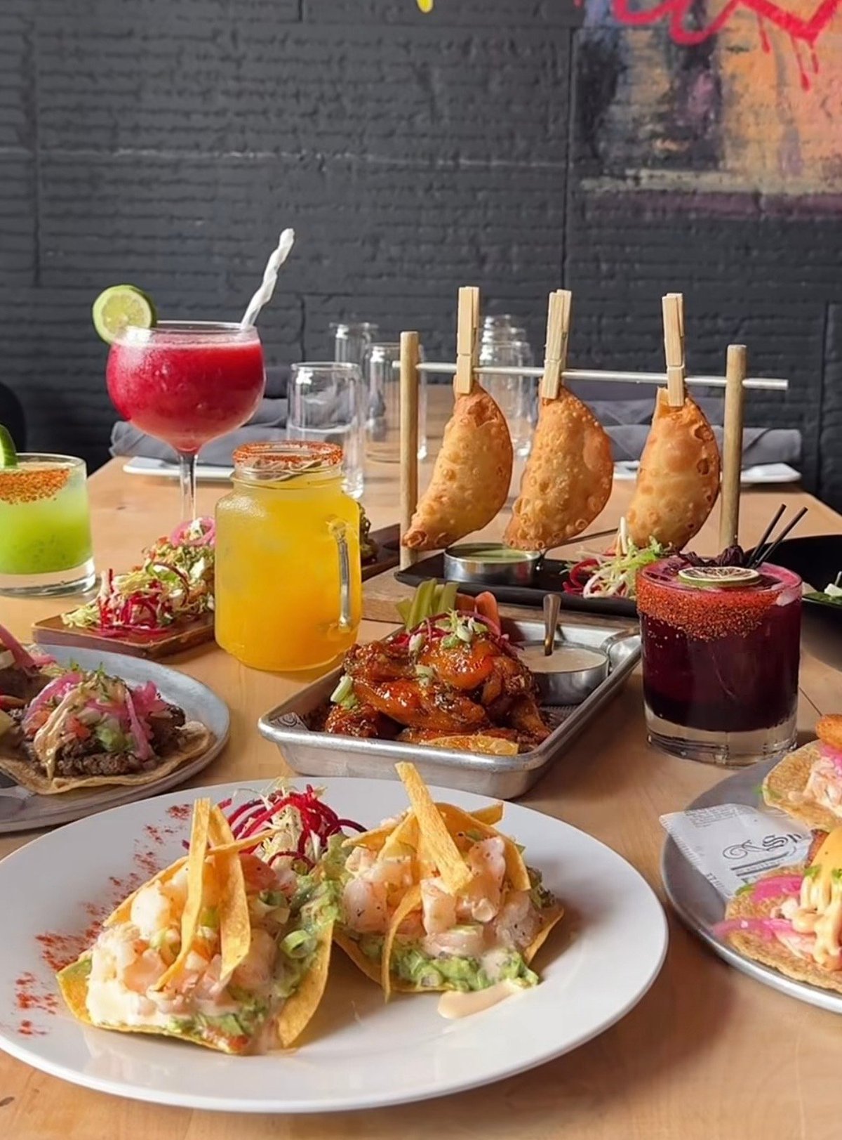 Upscale tapas spread with gourmet tacos, fried pear appetizers, colorful cocktails, and small plates on wooden table