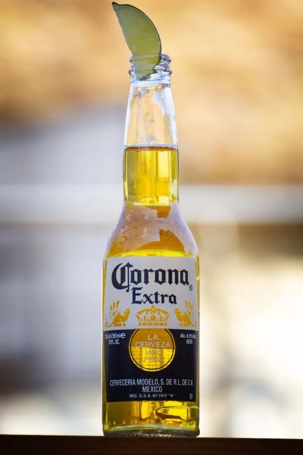 Corona Extra beer bottle with a fresh lime wedge on top against a blurred golden background