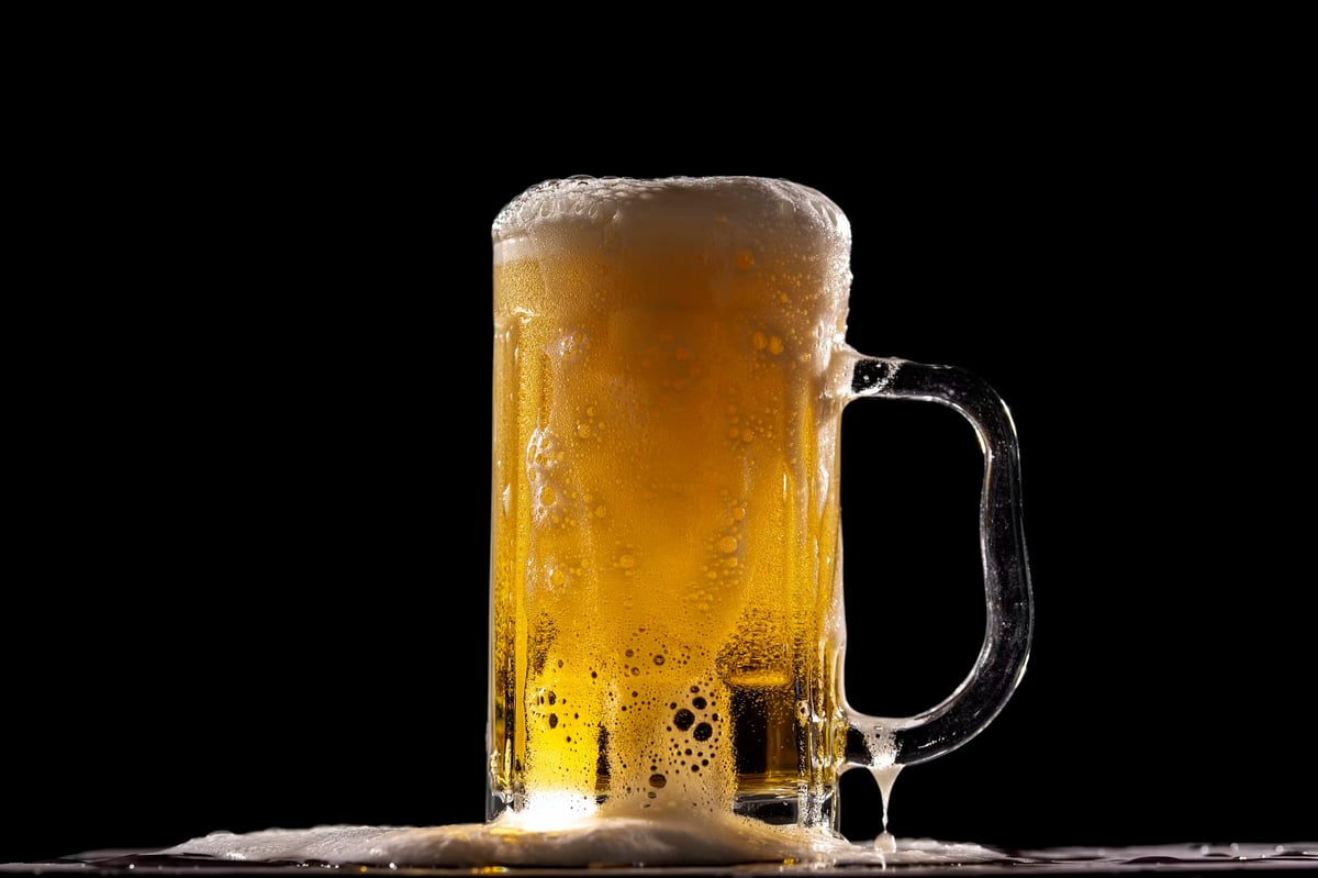 Frosty glass mug of golden beer with white foam head on a black background