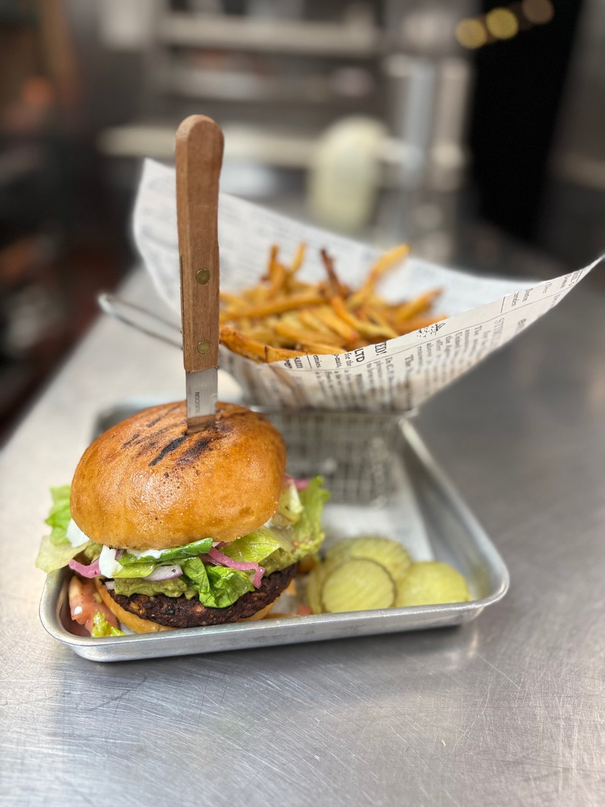 Gourmet burger on white paper container with wooden pick, served alongside french fries and cucumber slices