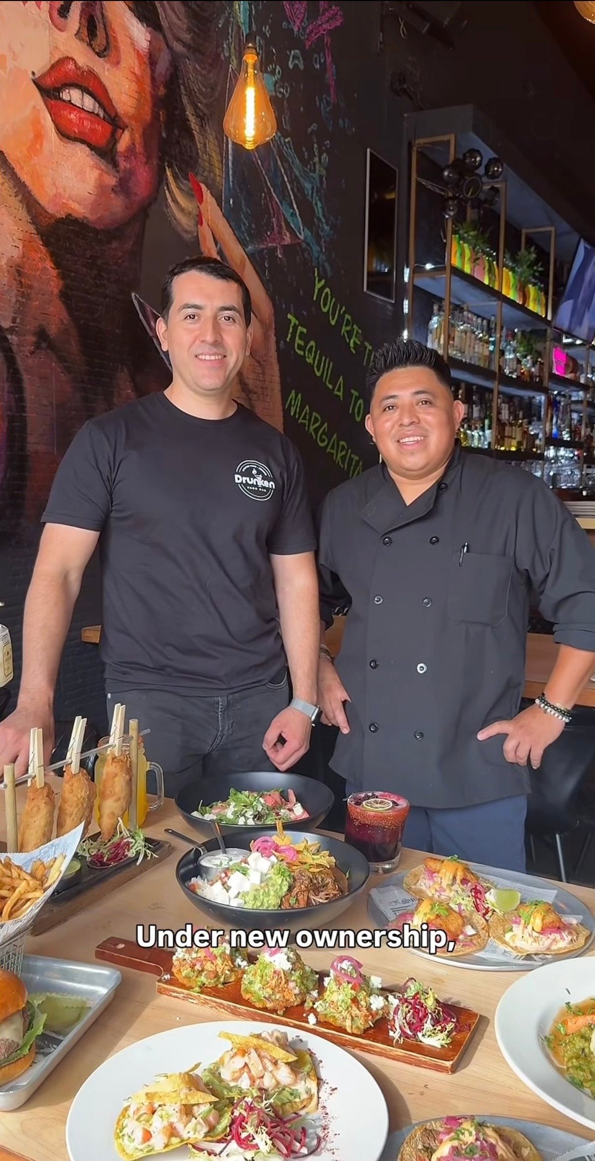 Owners Carlos Garcia and Fredy Duarte standing together behind a counter of signature Drunken Taco Bar dishes