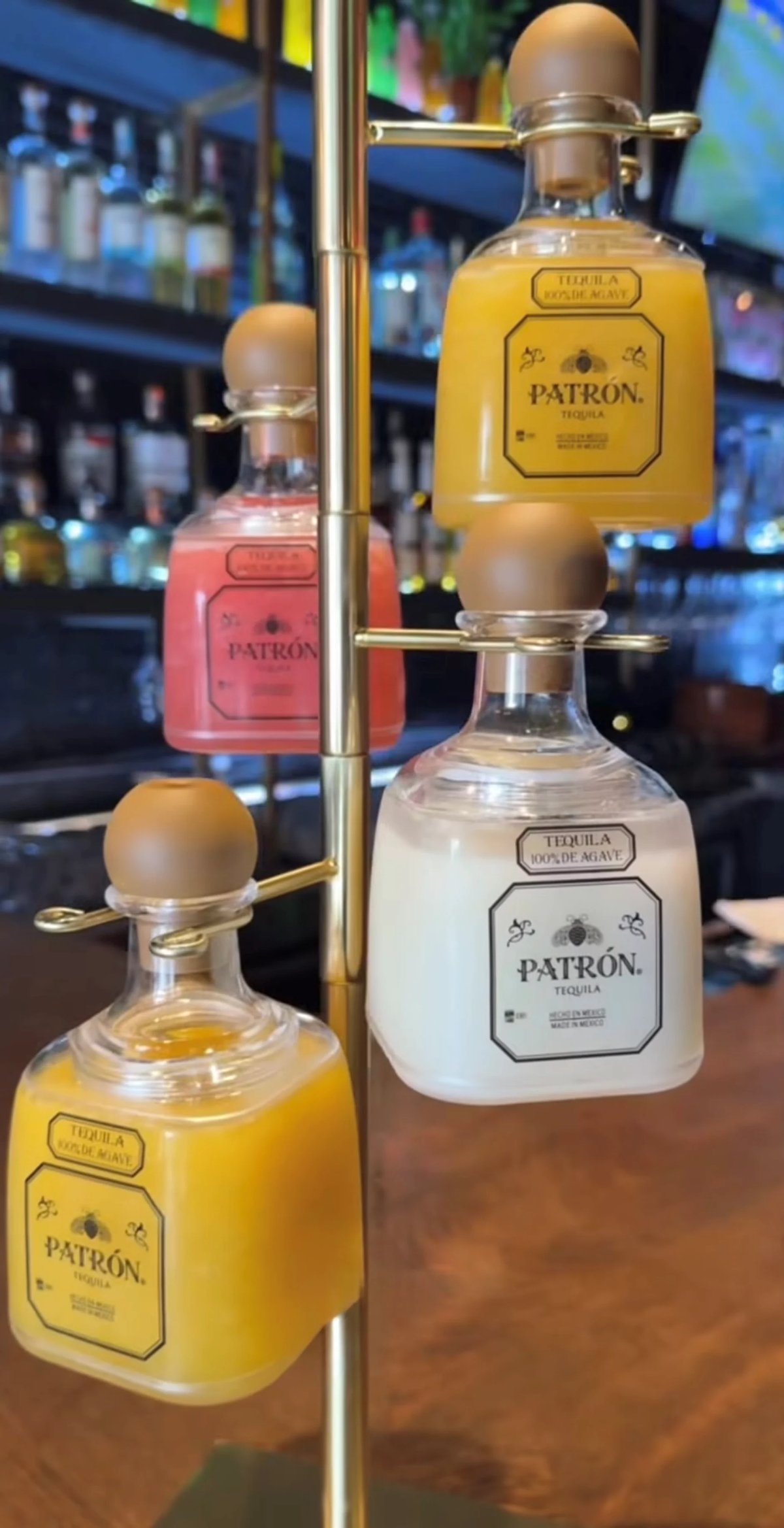 Three bottles of Patron tequila in different varieties displayed on a brass stand in a bar setting