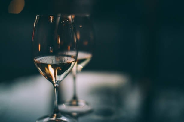 A glass of white wine with warm golden light reflecting through the liquid against a dark teal blurred background