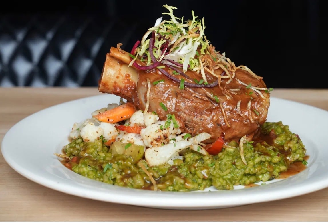 Grilled steak with green herb risotto, crispy crouton, shredded garnish, and white cream sauce on white plate