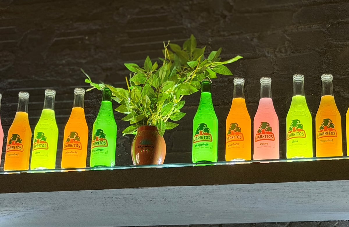 Row of colorful Mexican Jarritos soda bottles in mandarin, lime, grapefruit, guava, and passion fruit flavors on a wooden shelf