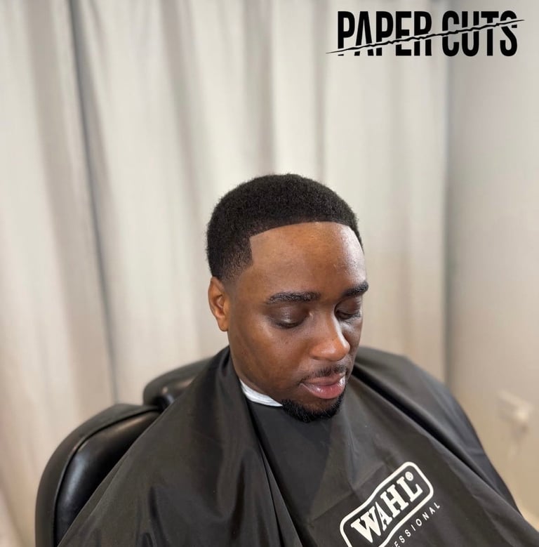 Man with freshly trimmed short black hair wearing a black barber cape with WAHL logo, sitting in barber chair