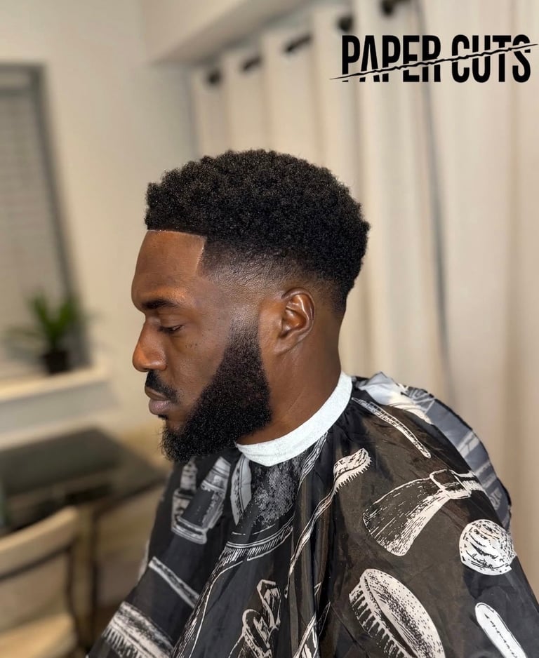 Man with high fade haircut and full beard shown in profile view wearing a patterned black shirt