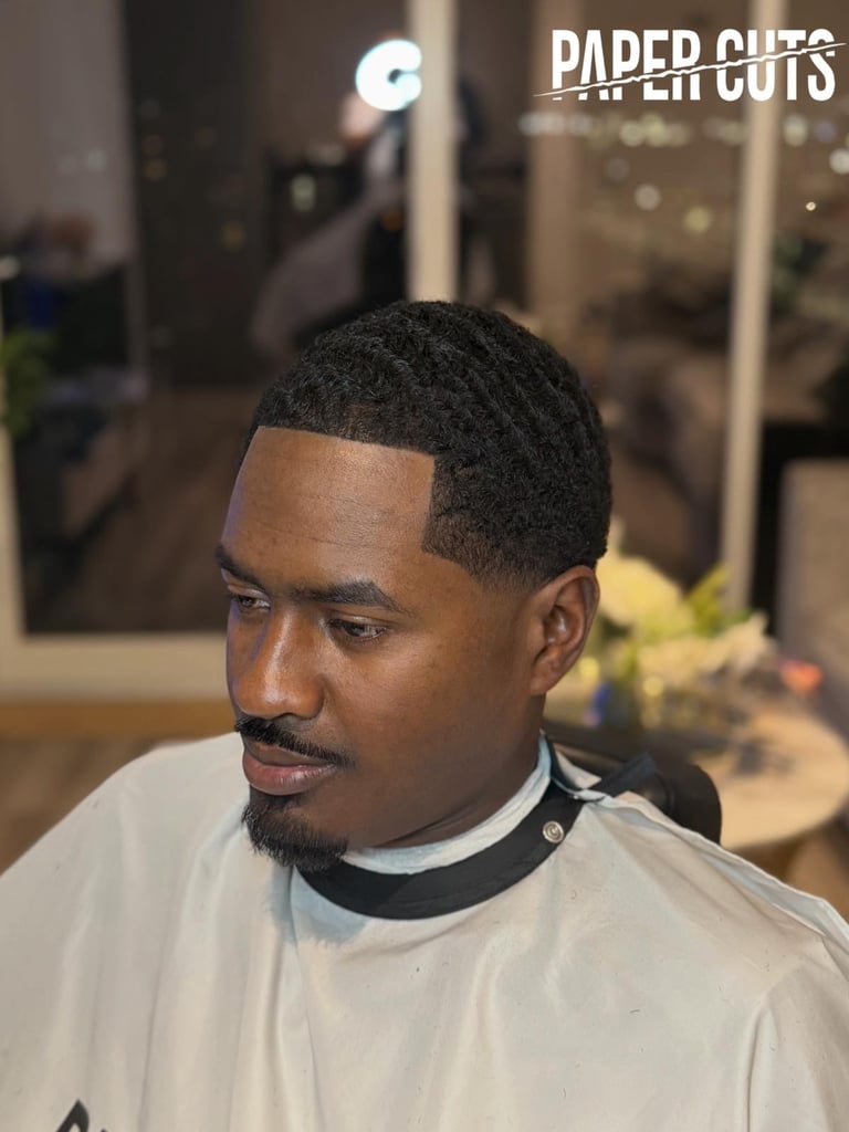 Man with fresh fade haircut wearing light colored shirt in barber shop with Paper Cuts logo visible