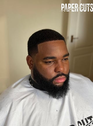Paper Cuts member with a short fade haircut and thick black beard