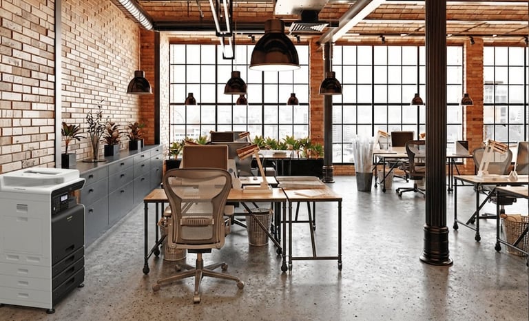 Modern industrial office space with brick walls, large windows, wooden desks, pendant lighting, and support columns