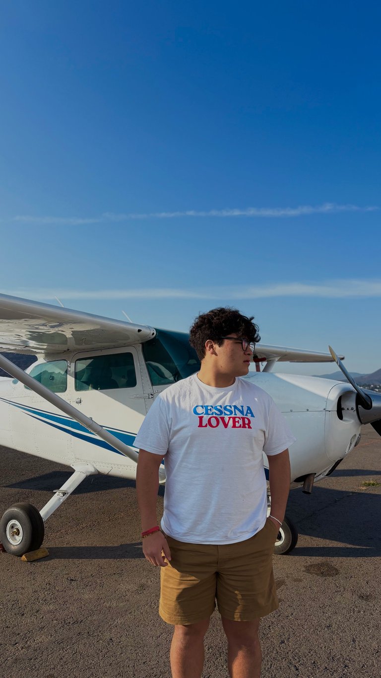 Young man wearing Cessna Lover t-shirt standing in front of a white Cessna aircraft on runway