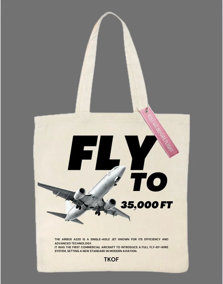 Cream canvas tote bag with black airplane graphic and FLY TO 35,000FT text, featuring a pink luggage tag