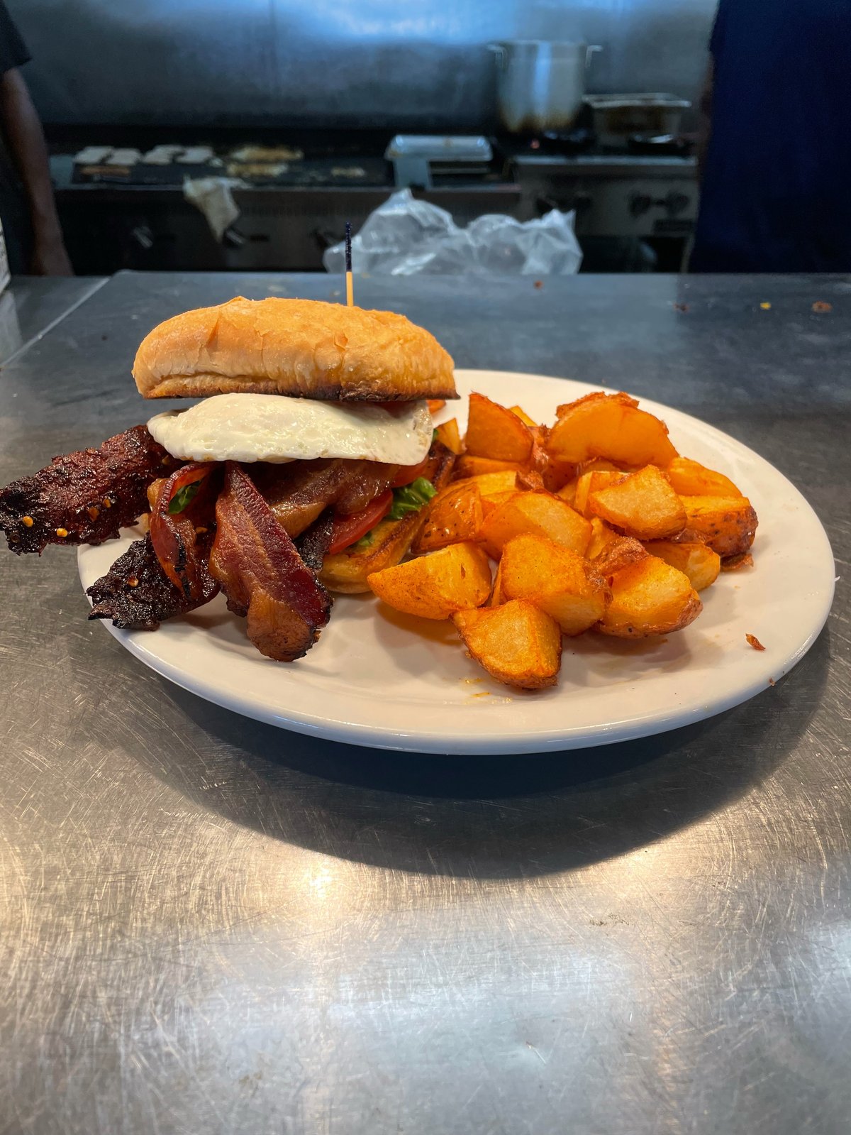 Plate with cheeseburger, crispy bacon, and orange roasted potatoes in a commercial kitchen