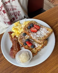 French toast topped with powdered sugar and fresh strawberries, served with bacon