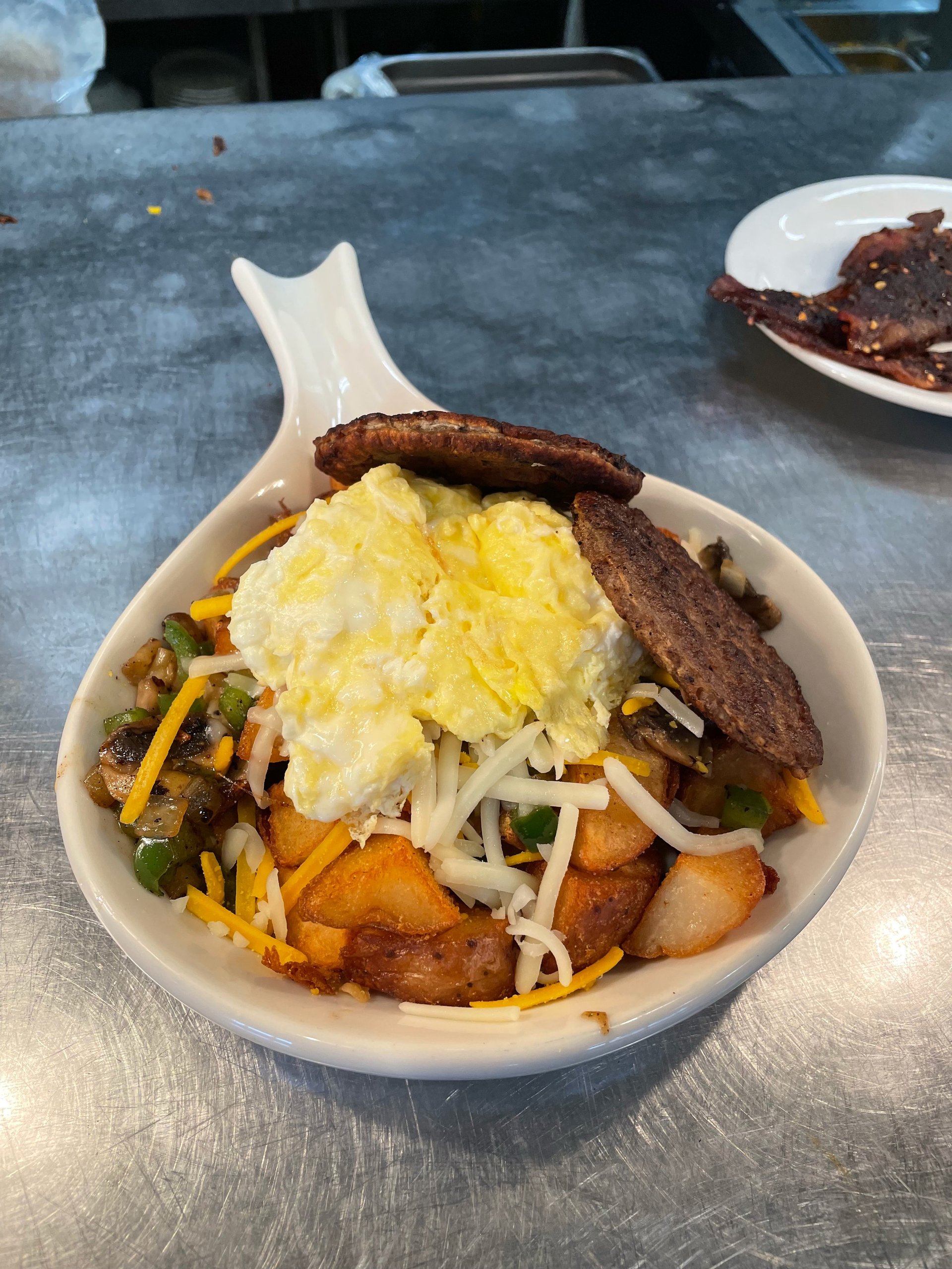 Breakfast bowl with eggs, potatoes, cheese, green onions, sausage and toast in white paddle dish