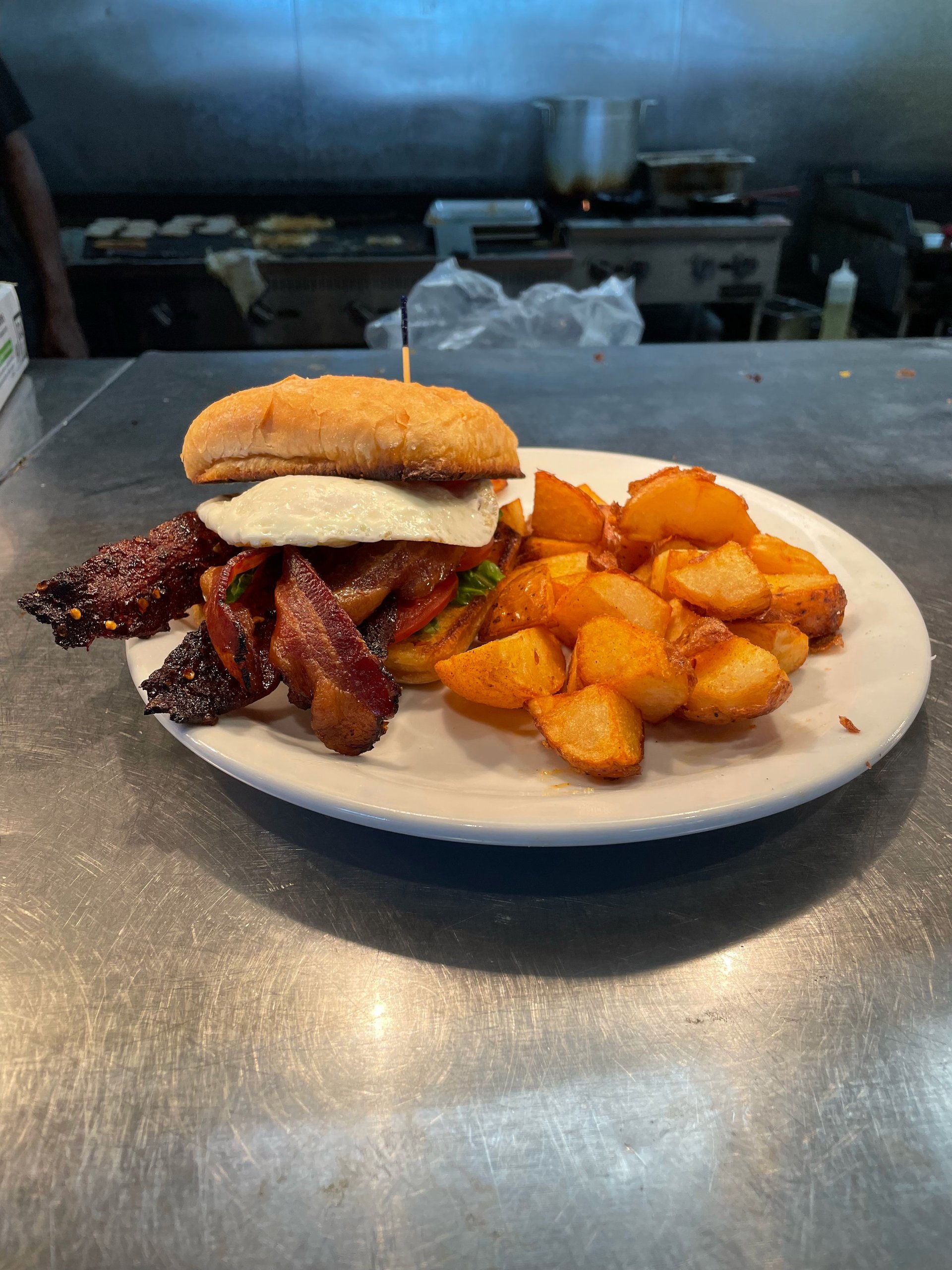 A plate with a chicken sandwich, crispy bacon strips, and golden roasted potatoes