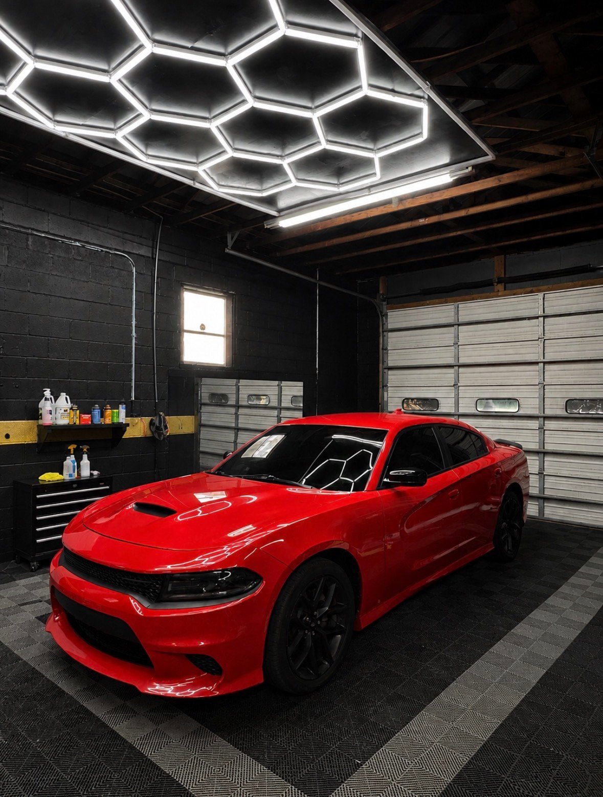 Red Dodge Charger parked in modern garage with hexagonal LED ceiling lights and tool storage