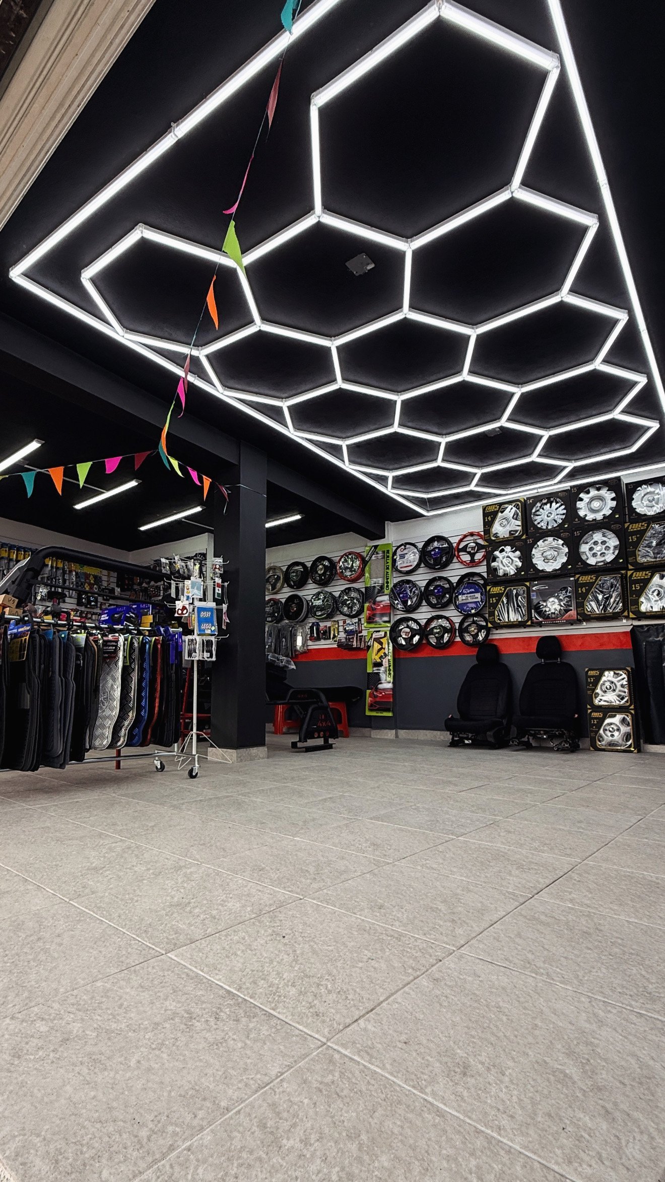 Interior del showroom de Suki Motors — techo con luces LED hexagonales, racks de accesorios y exhibidores de rines