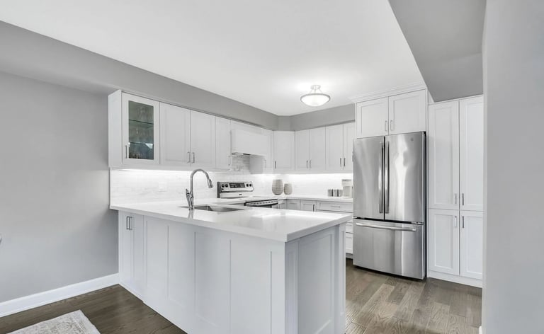 Modern white kitchen with island, stainless steel appliances, and light wood flooring