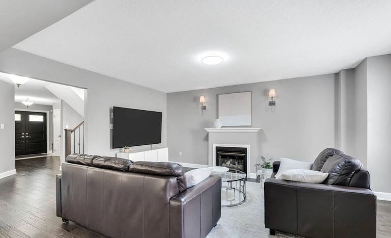 Modern living room with gray leather furniture, flat-screen TV above fireplace, recessed ceiling lights, and hardwood floors
