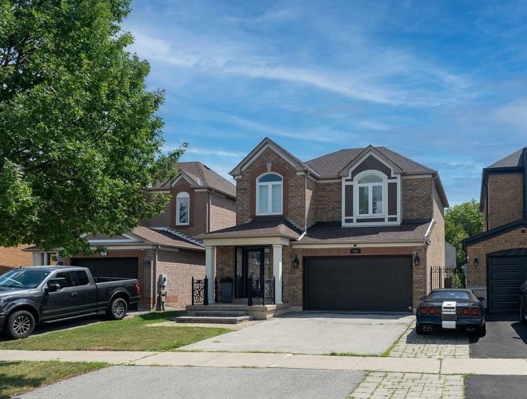 Modern brick two-story residential home with dark roof, two-car garage, and mature trees under blue sky