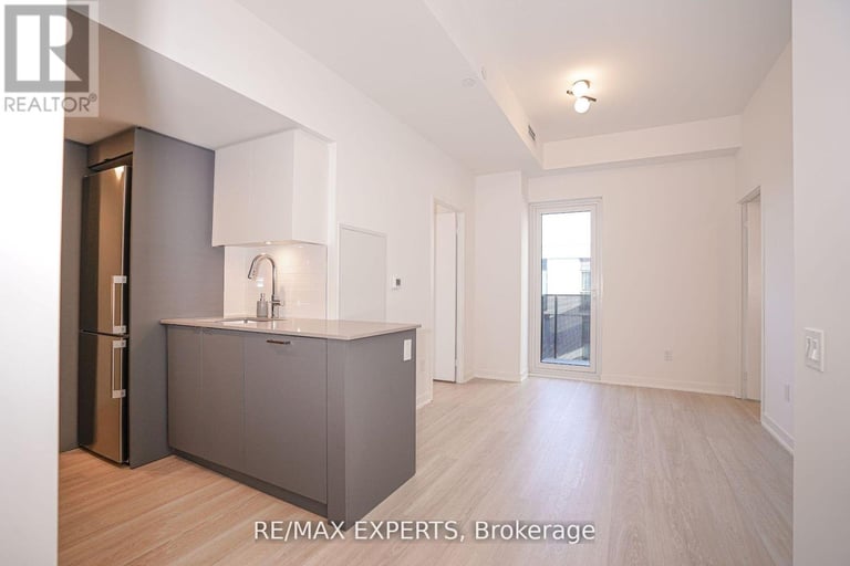 Open-concept living and kitchen with gray cabinetry, light wood flooring, and bright natural light