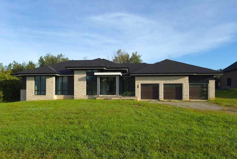 Modern single-story house with beige brick and black roof on expansive green lawn with trees in background
