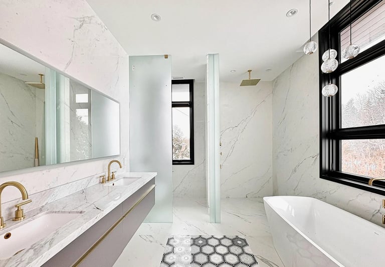 Modern luxury bathroom with marble surfaces, floating double vanity with brass faucets, glass shower enclosure, white soaking tub, and geometric floor tiles