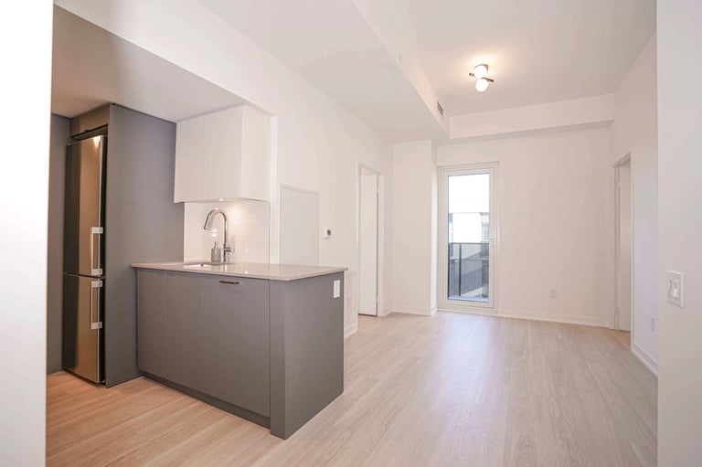 Modern open-concept kitchen and living area with dark gray island, light wood flooring, and bright white walls