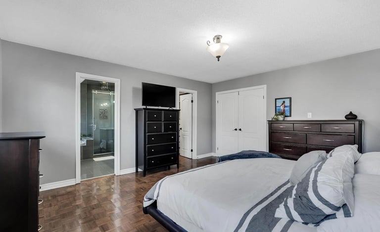 Spacious master bedroom with queen bed, dark wood furniture, glass-door bathroom, and hardwood flooring